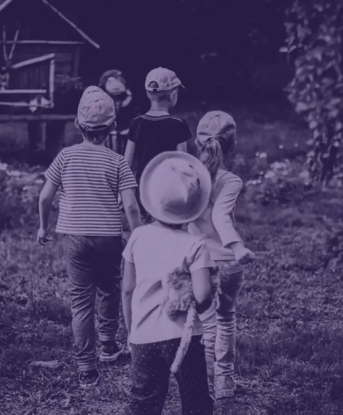 Piątka dzieci, które idą w ogrodzie w stronę małego drewnianego domku.